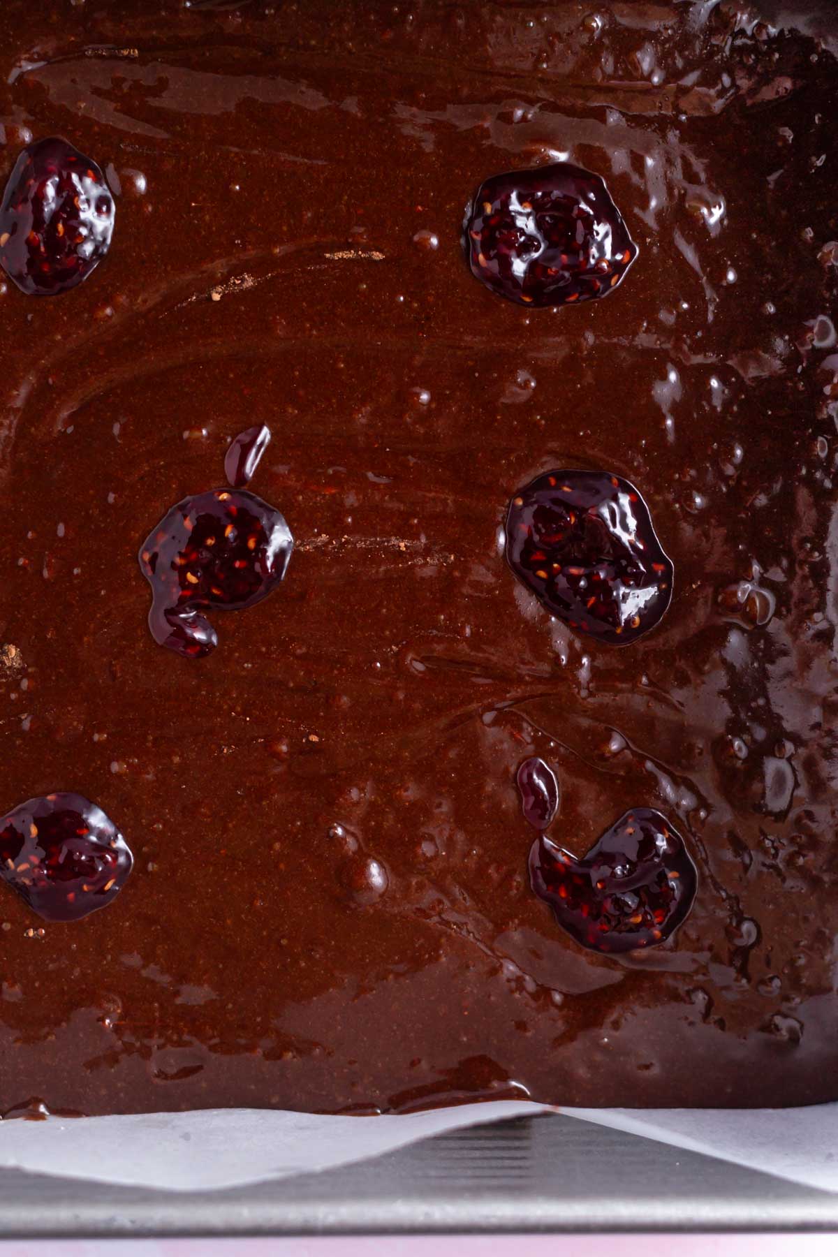 brownie batter in a baking tin with raspberry jam dolloped over the top.