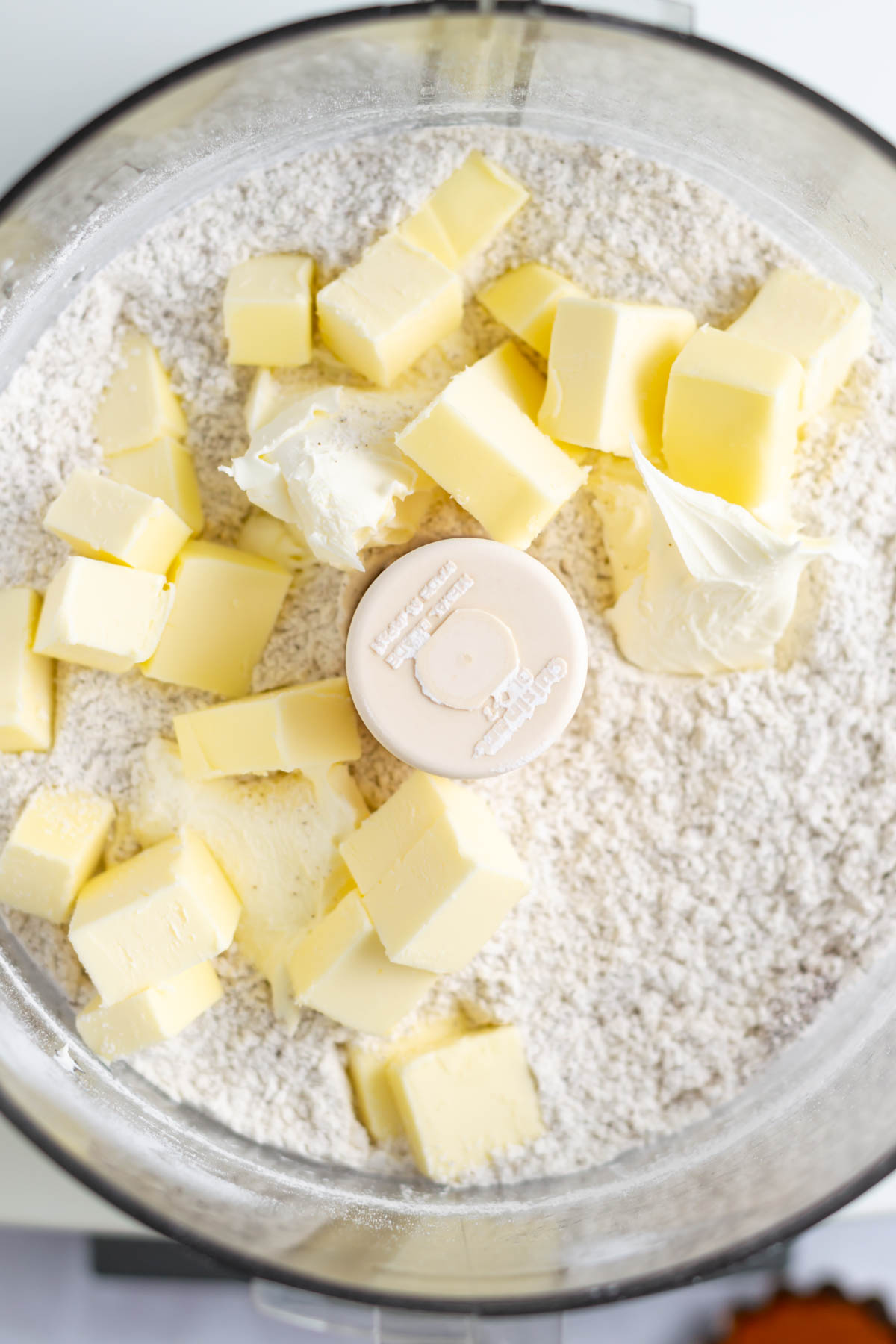 cubes of butter and mascarpone cheese added to dry ingredients in a food processor bowl
