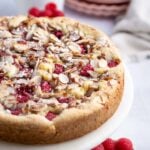 raspberry almond cake on a cake stand with plates in the background