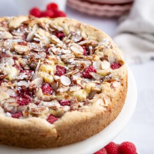 raspberry almond cake on a cake stand with plates in the background
