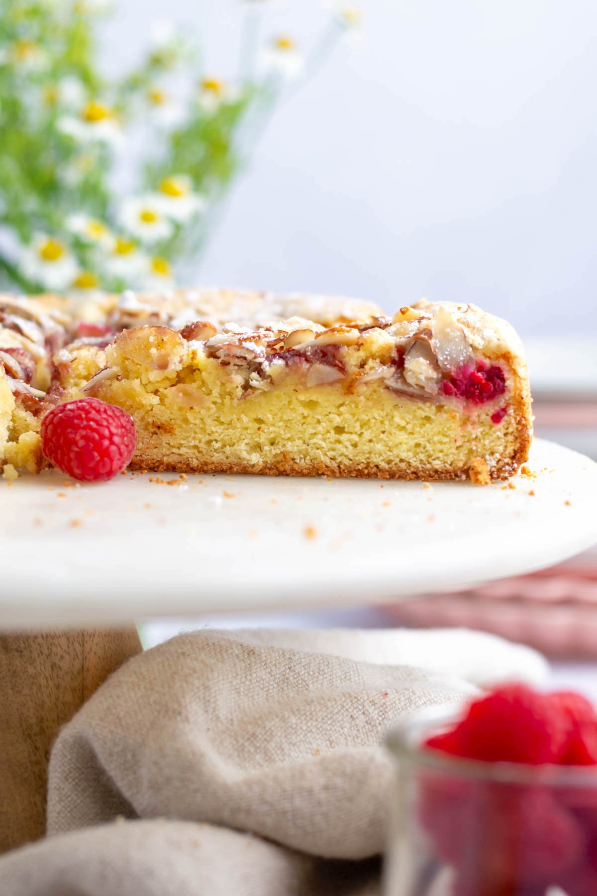 sliced cake on a cake stand with fresh raspberries and flowers in the background