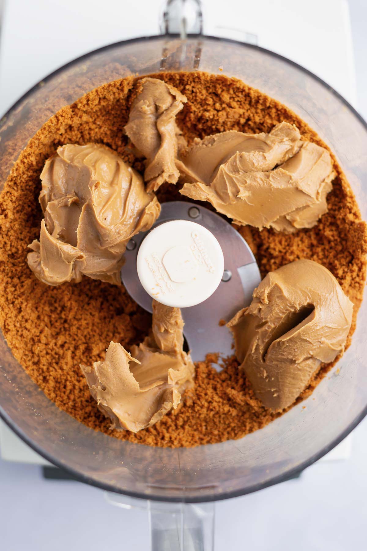 cookie butter spread added to cookie crumbs in the bowl of a food processor