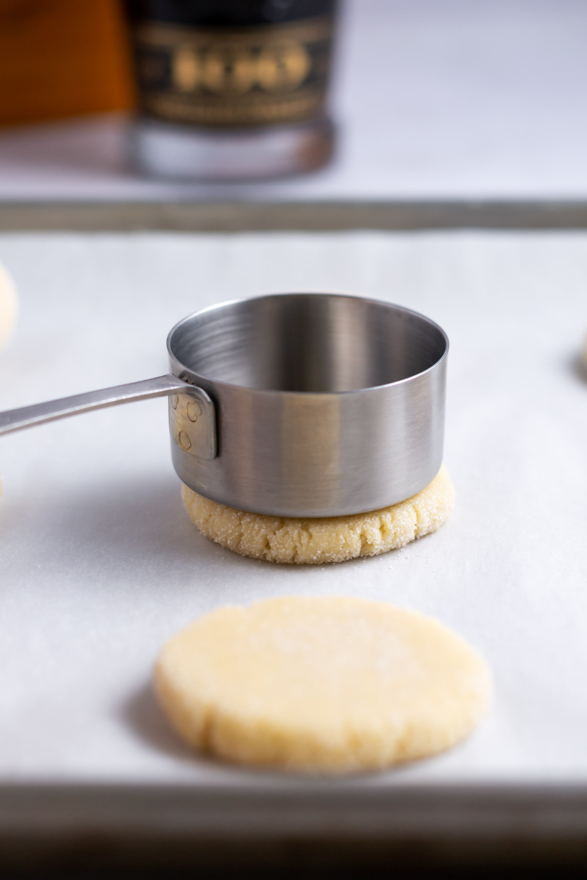 measuring cup pressing cookie dough down on a parchment lined baking pan