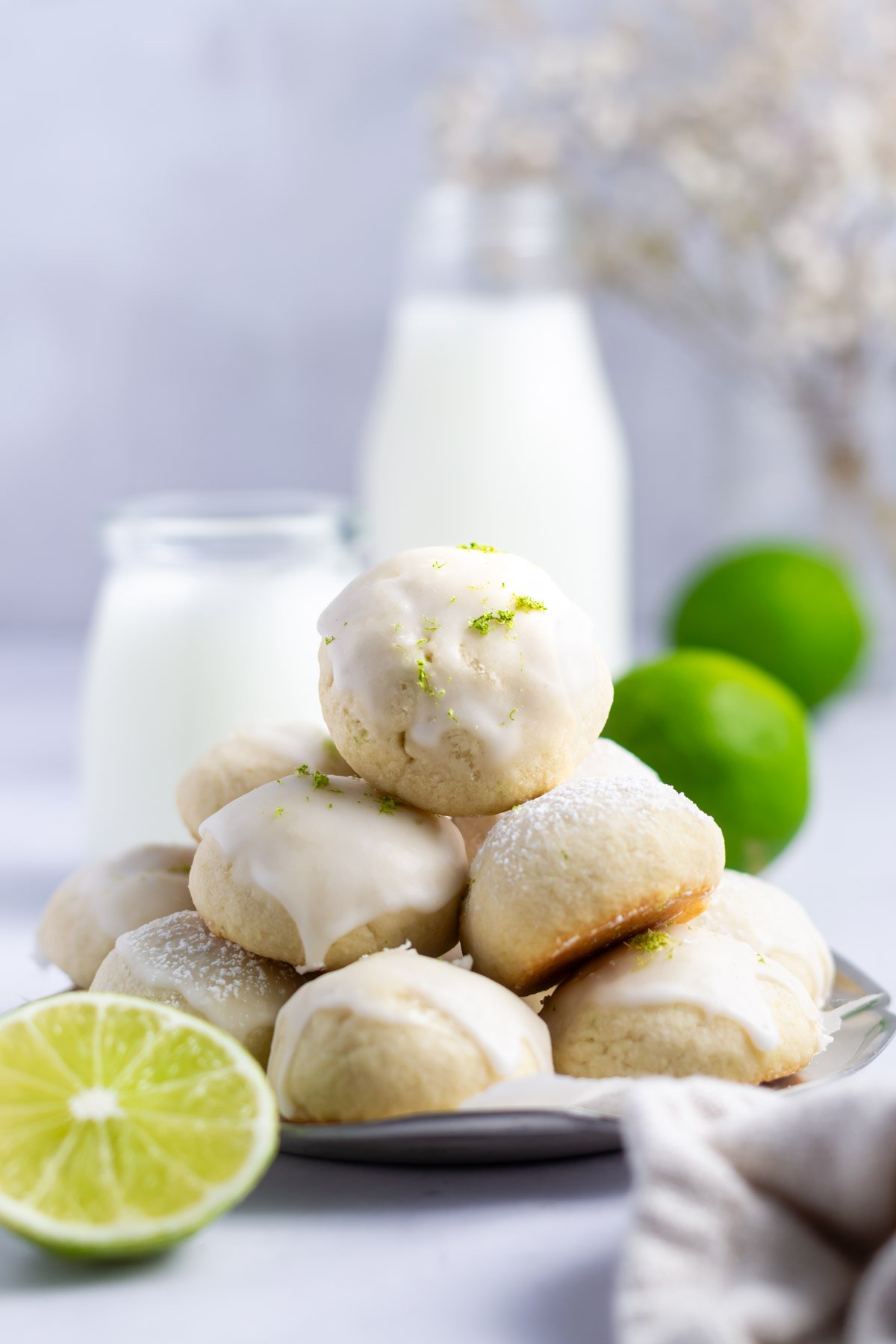 pile of lime cookies on a platter with milk and limes in the background