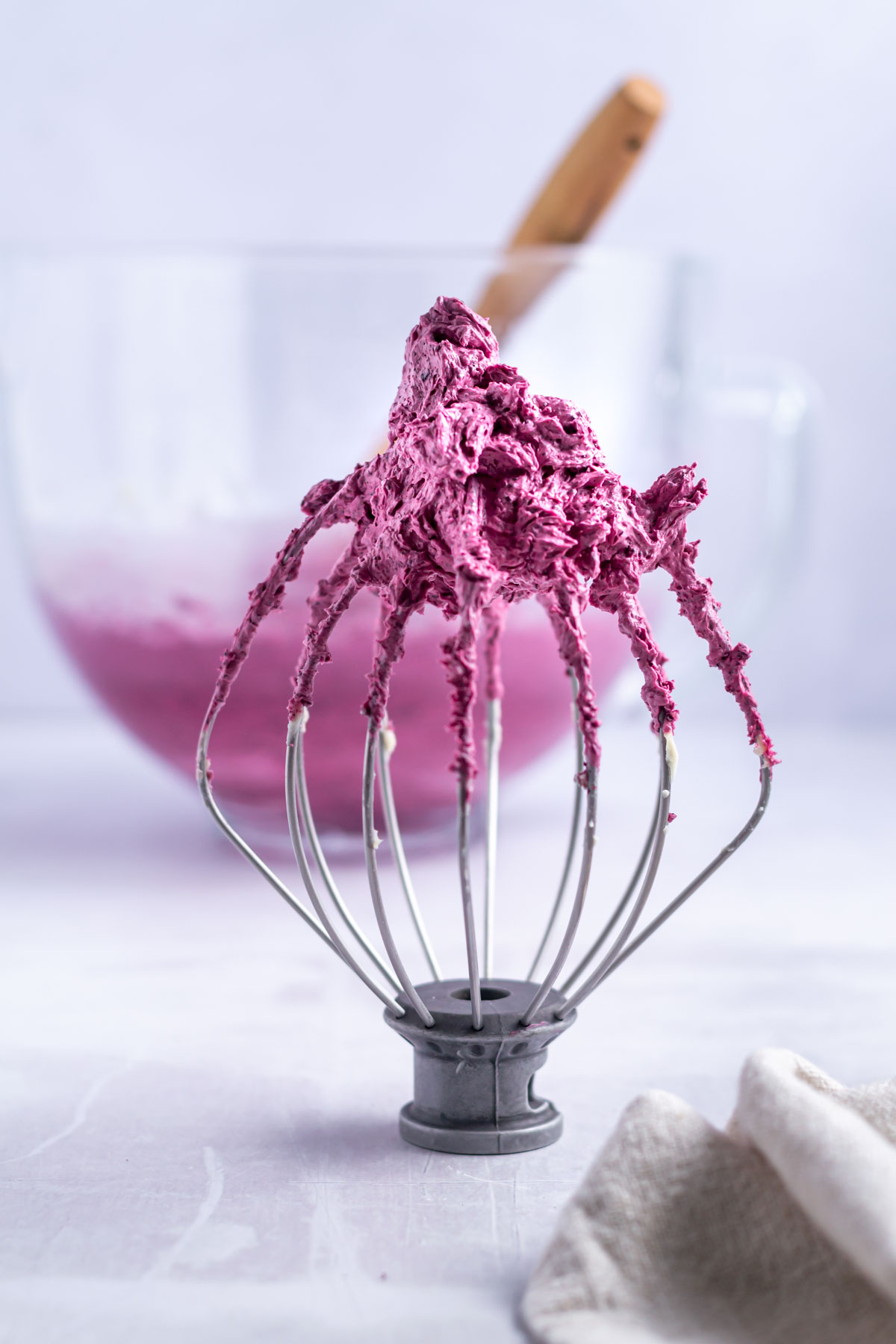 whisk with blueberry frosting on the top and a bowl of buttercream in the background