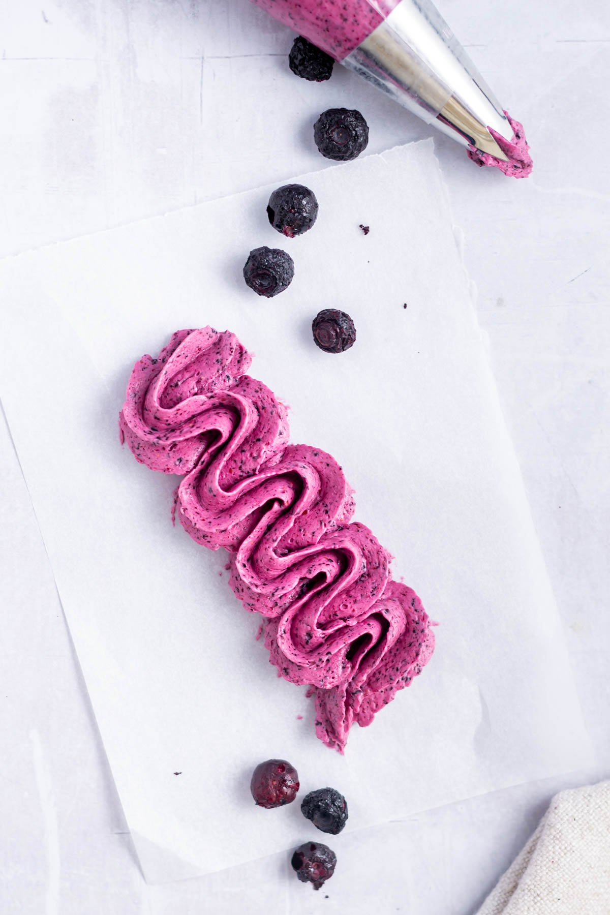 blueberry frosting piped on a piece of parchment paper with freeze dried berries