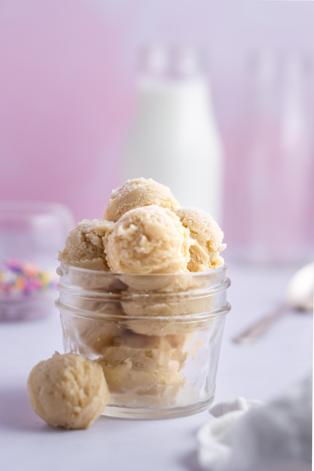 sugar cookie cookie dough in a jar with milk, sprinkles and a spoon in the background