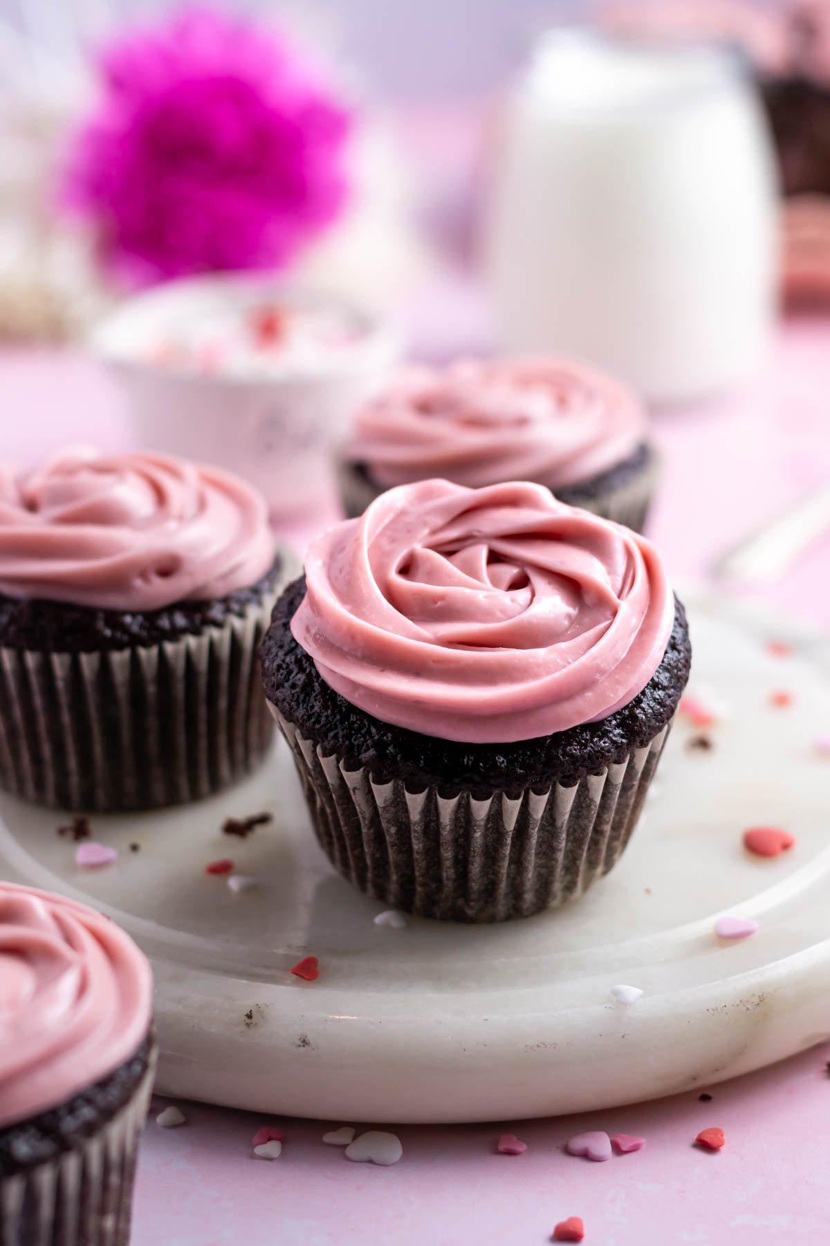 three chocolate cupcakes on a marble plate with a glass of milk