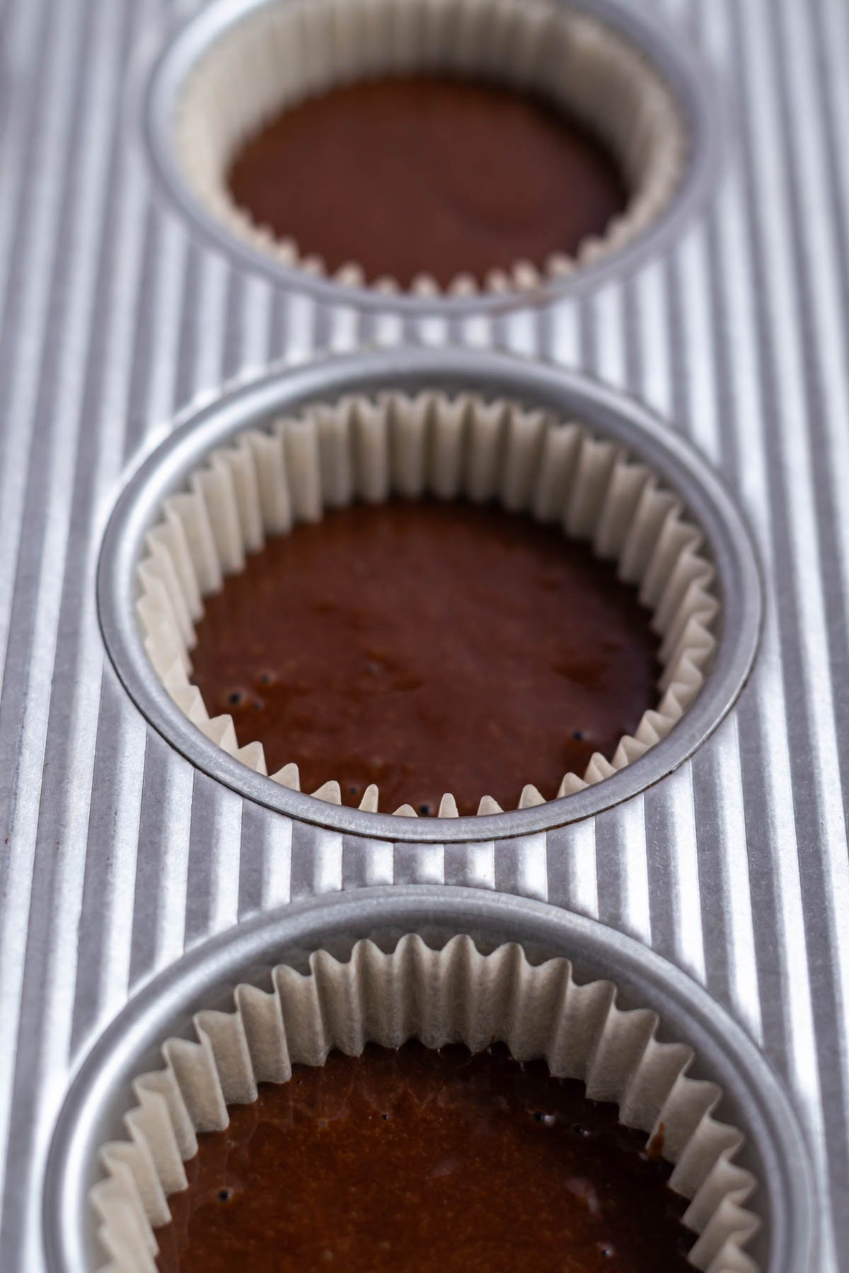 chocolate cupcake batter half filling liners in a muffin tin