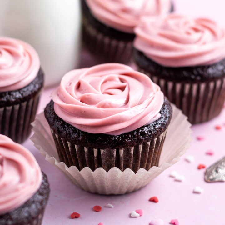 chocolate raspberry cupcakes with heart shaped sprinkles and a glass of milk in the background