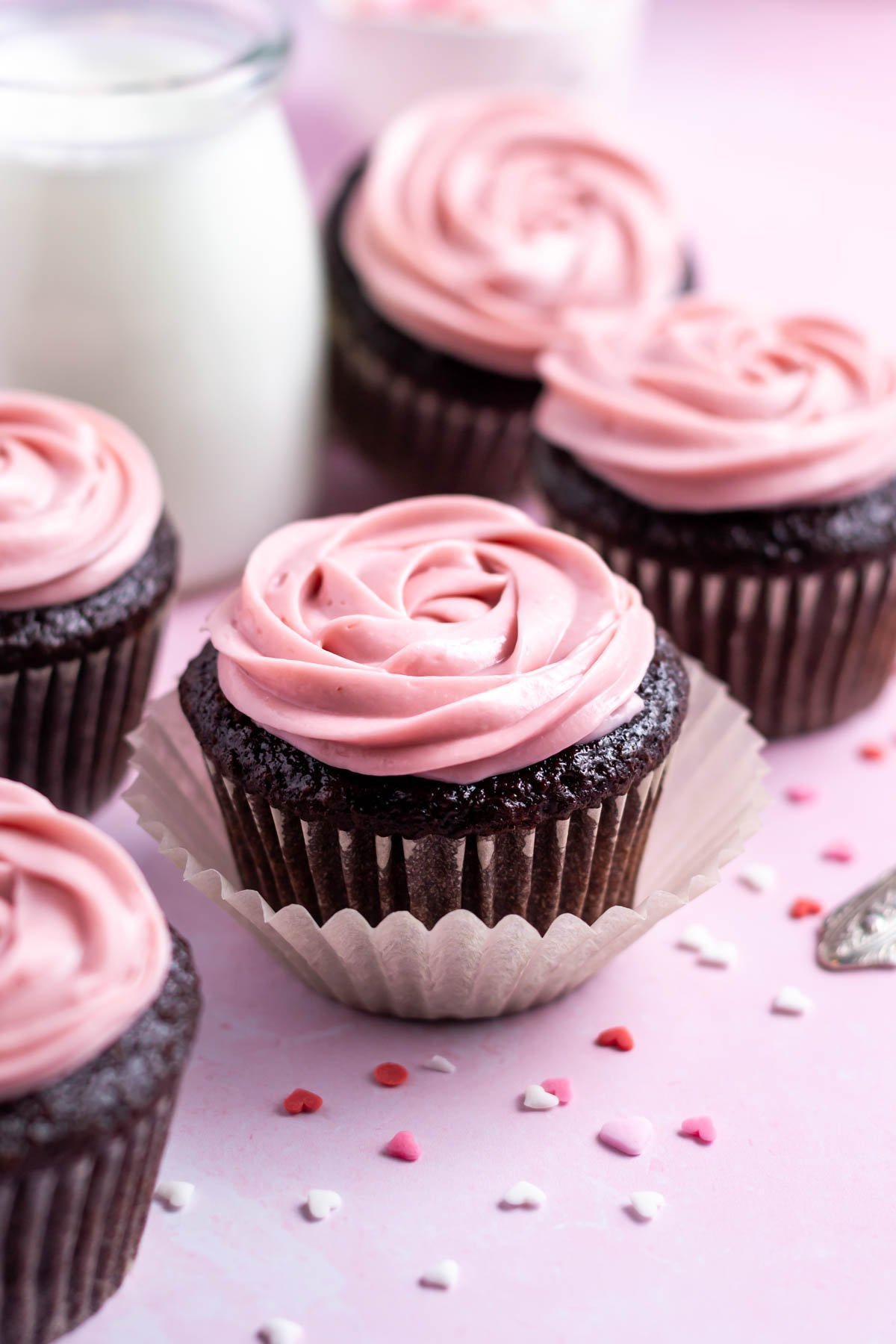 chocolate raspberry cupcakes with heart shaped sprinkles and a glass of milk in the background