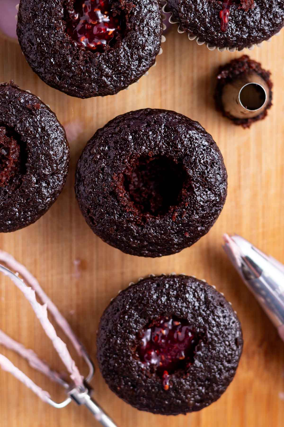 chocolate cupcakes on a cutting board with the centers removed; some are filled with raspberry jam