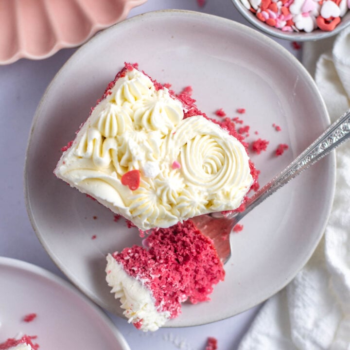 slice of pink velvet cake on a plate with a bite on a fork