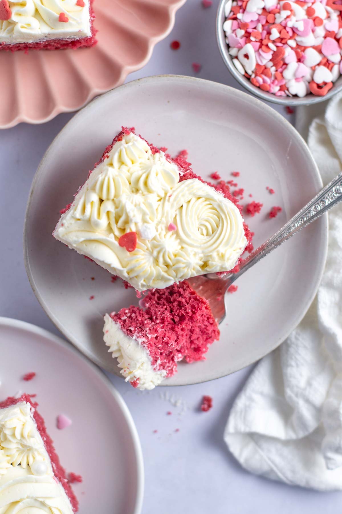 slice of pink velvet cake on a plate with a bite on a fork