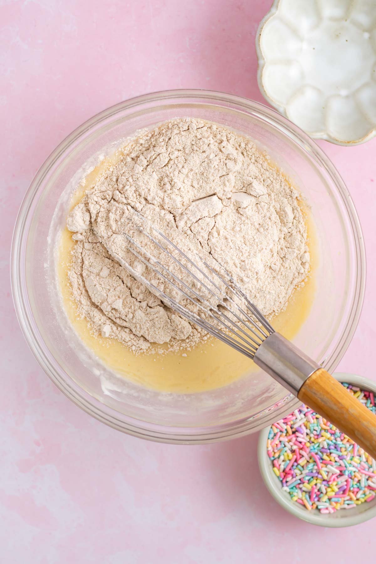 whole wheat flour added to wet ingredients in a bowl with a whisk