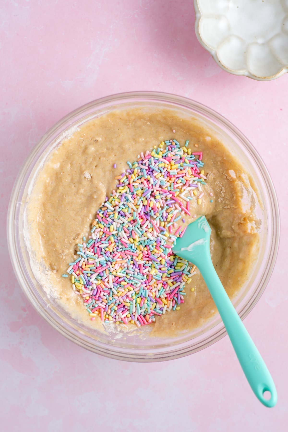 sprinkles added to donut batter in a bowl with a spatula.
