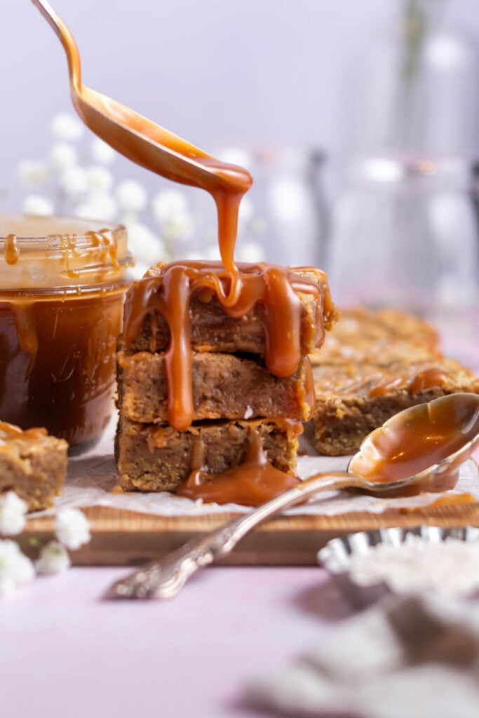 caramel being drizzled over the top of a stack of brownies