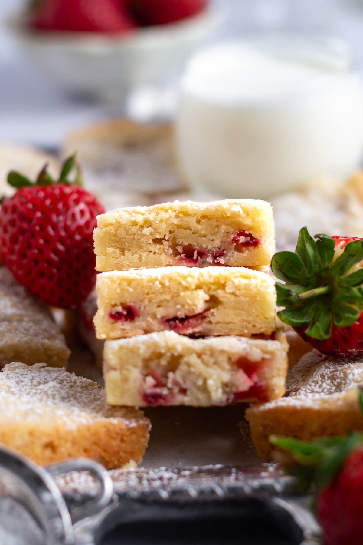 three strawberry blondies stacked on a serving tray with fresh strawberries
