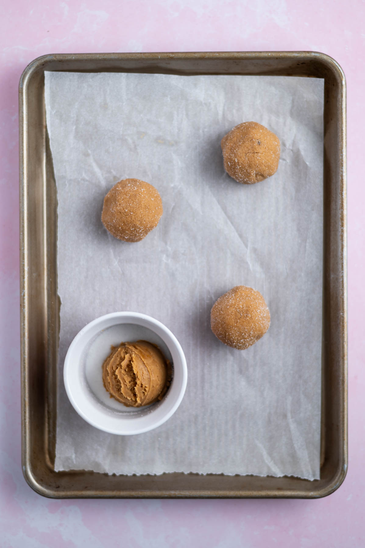 cookie dough balls on a parchment lined baking sheet; one cookie in a small bowl of granulated sugar