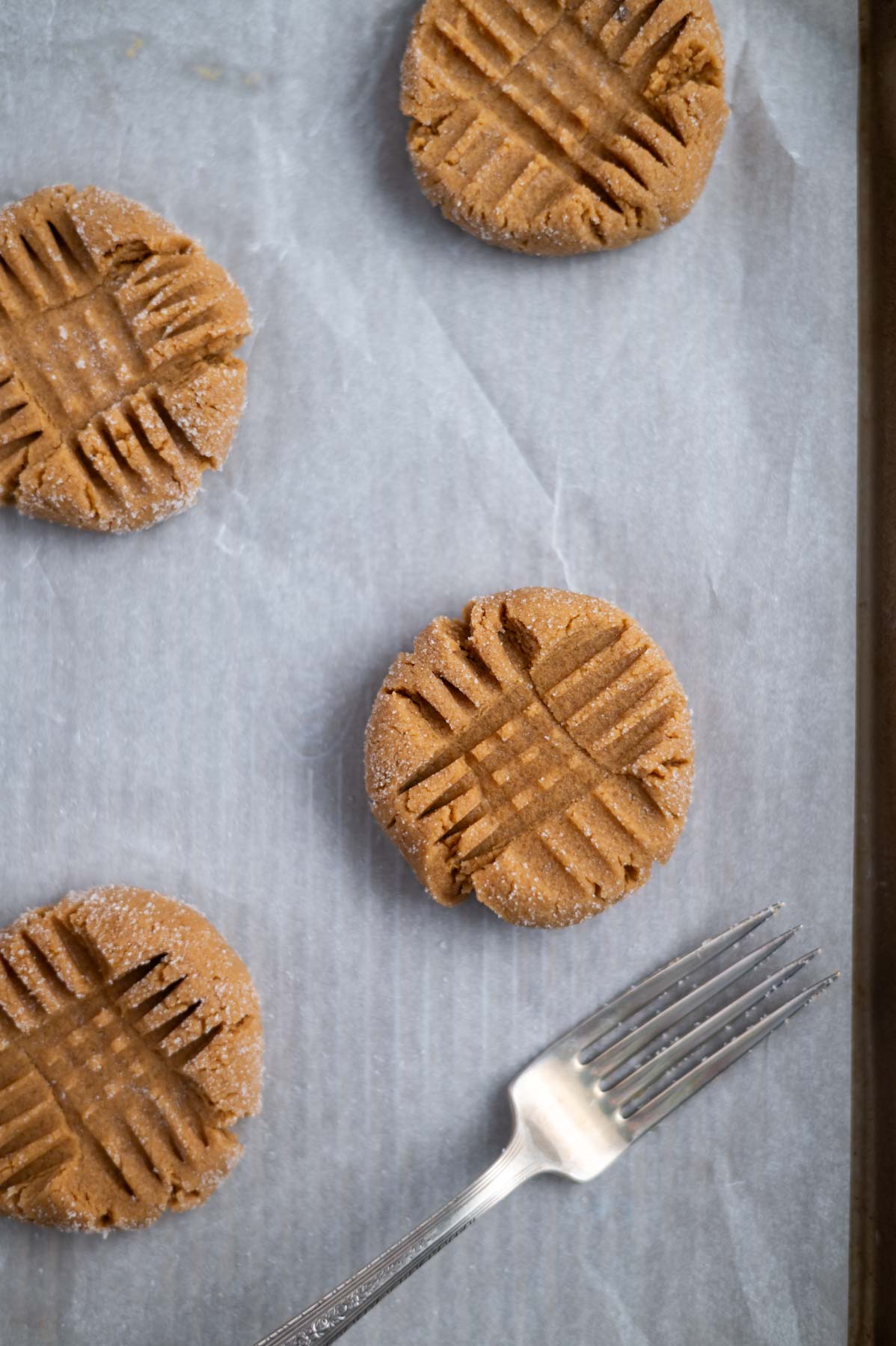 peanut butter cookies on a parchment lined baking sheet with crisscross marks