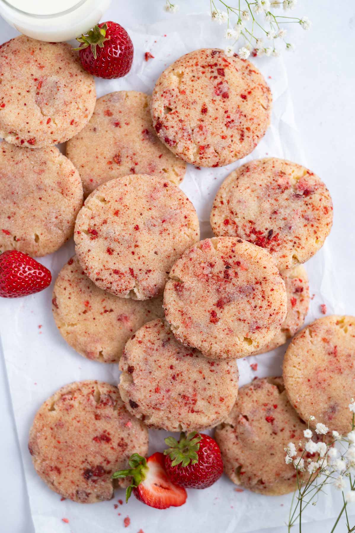 pile of cookies on parchment paper with fresh strawberries and a glass of milk