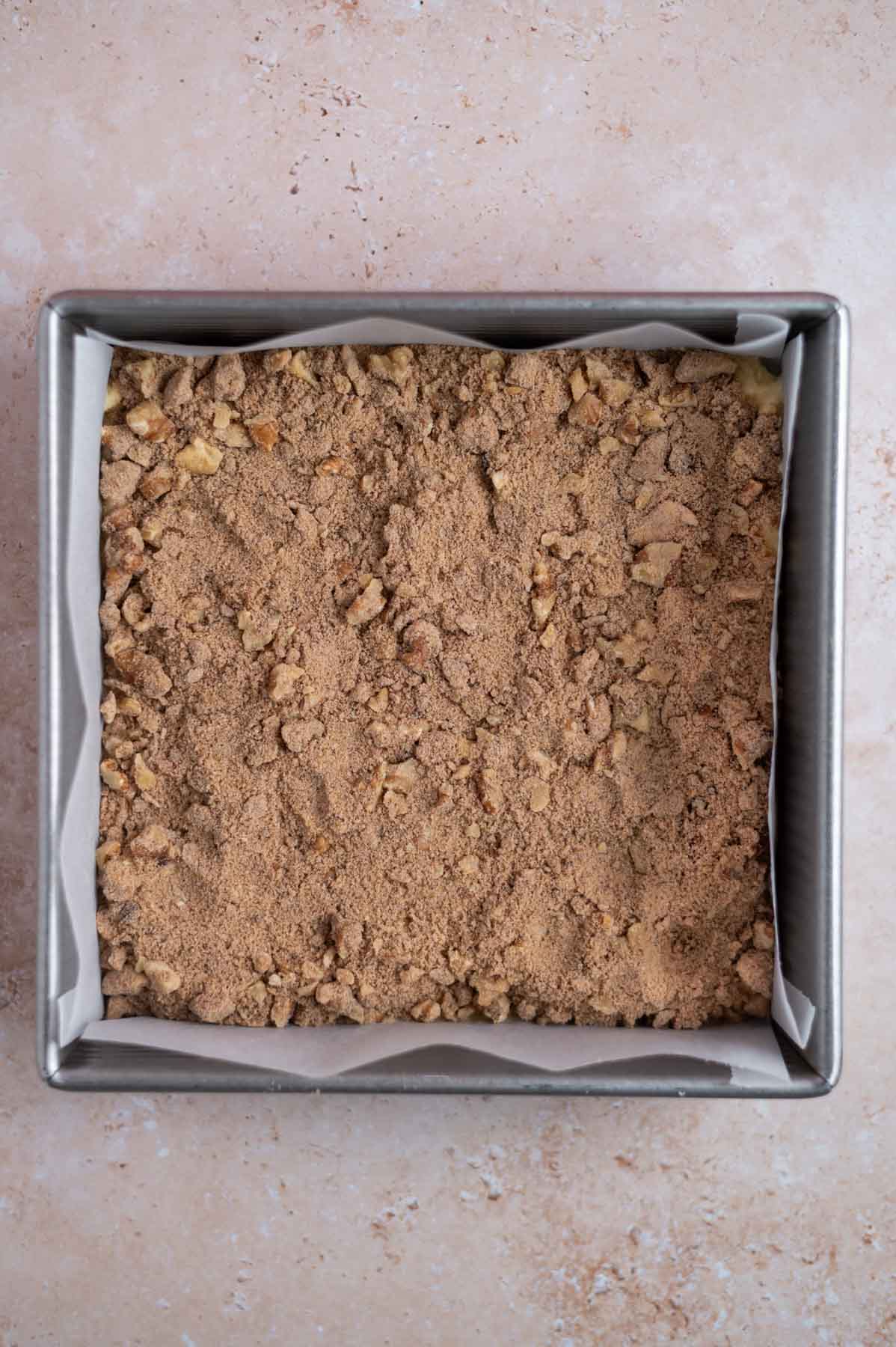 streusel layer over cake batter in a parchment lined baking pan