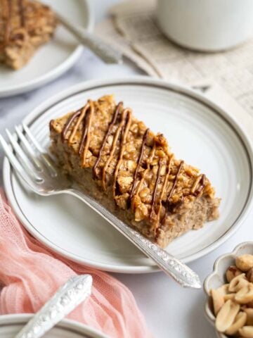 slice of baked peanut butter oatmeal on a plate with a fork. A bowl of peanuts and coffee sitting nearby.