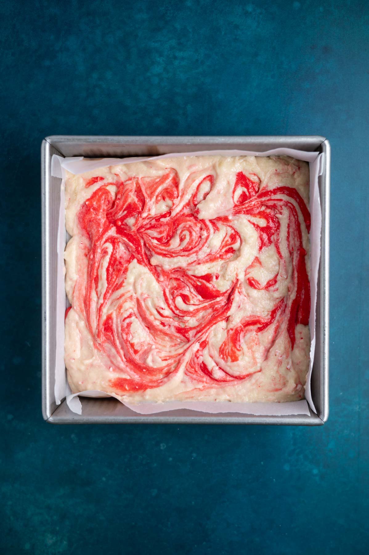 red cake batter swirled into vanilla batter in a parchment lined baking pan