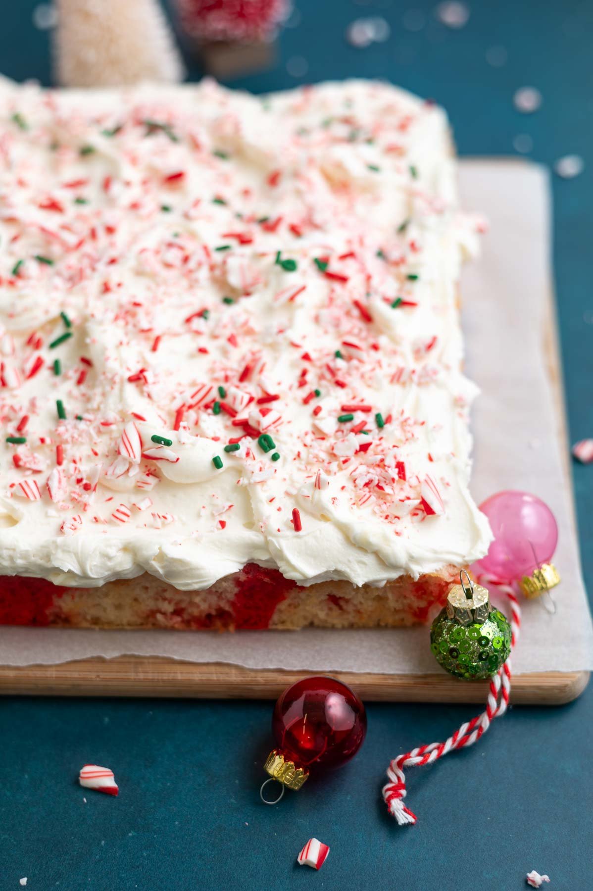 buttercream frosted candy cane cake on a parchment lined cutting board with Christmas ornaments