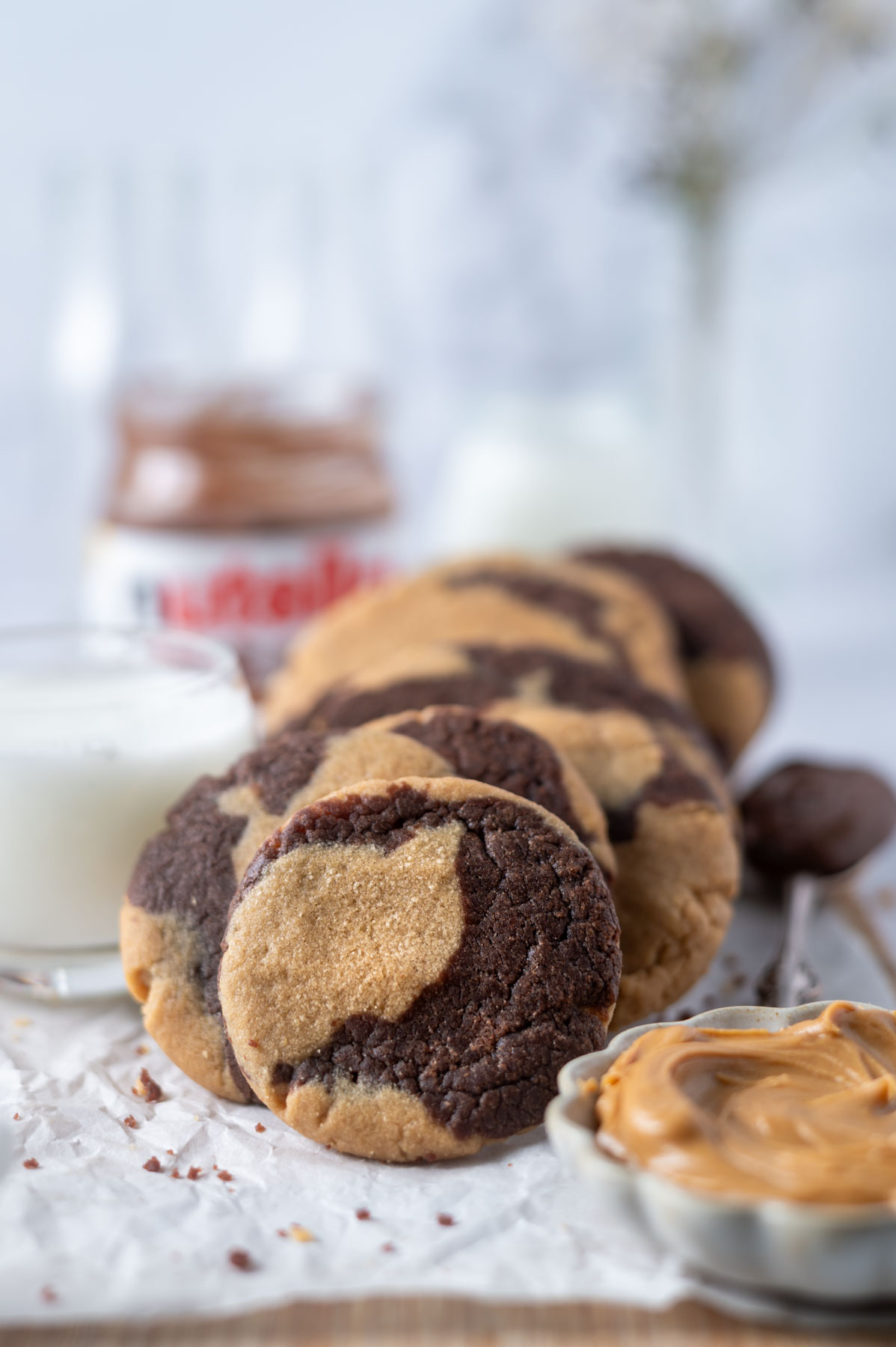 peanut butter nutella cookies on a parchment lined cutting board with a glass of milk and a jar of nutella