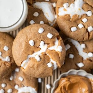 baked peanut butter marshmallow cookies on a baking pan with a bowl of peanut butter and a glass of milk