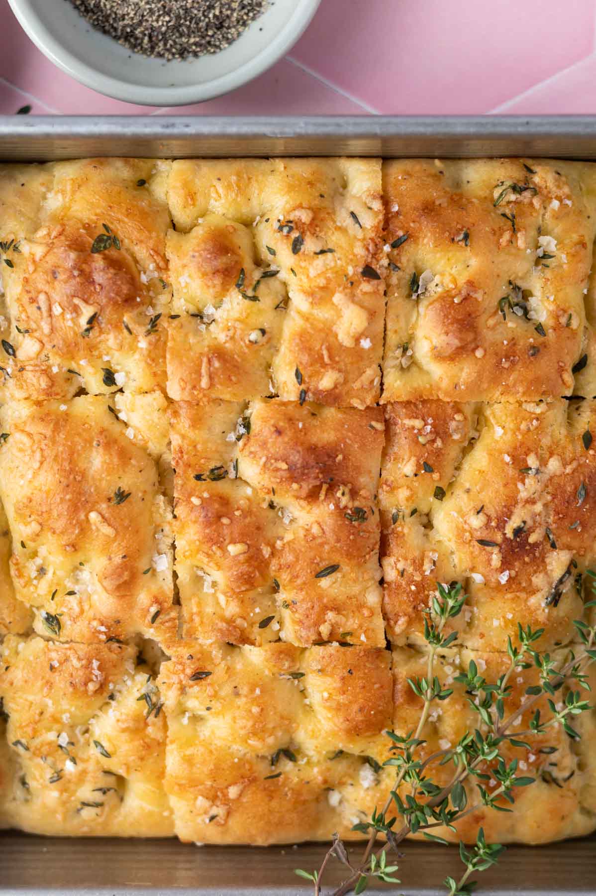 baked focaccia in a baking pan with fresh thyme