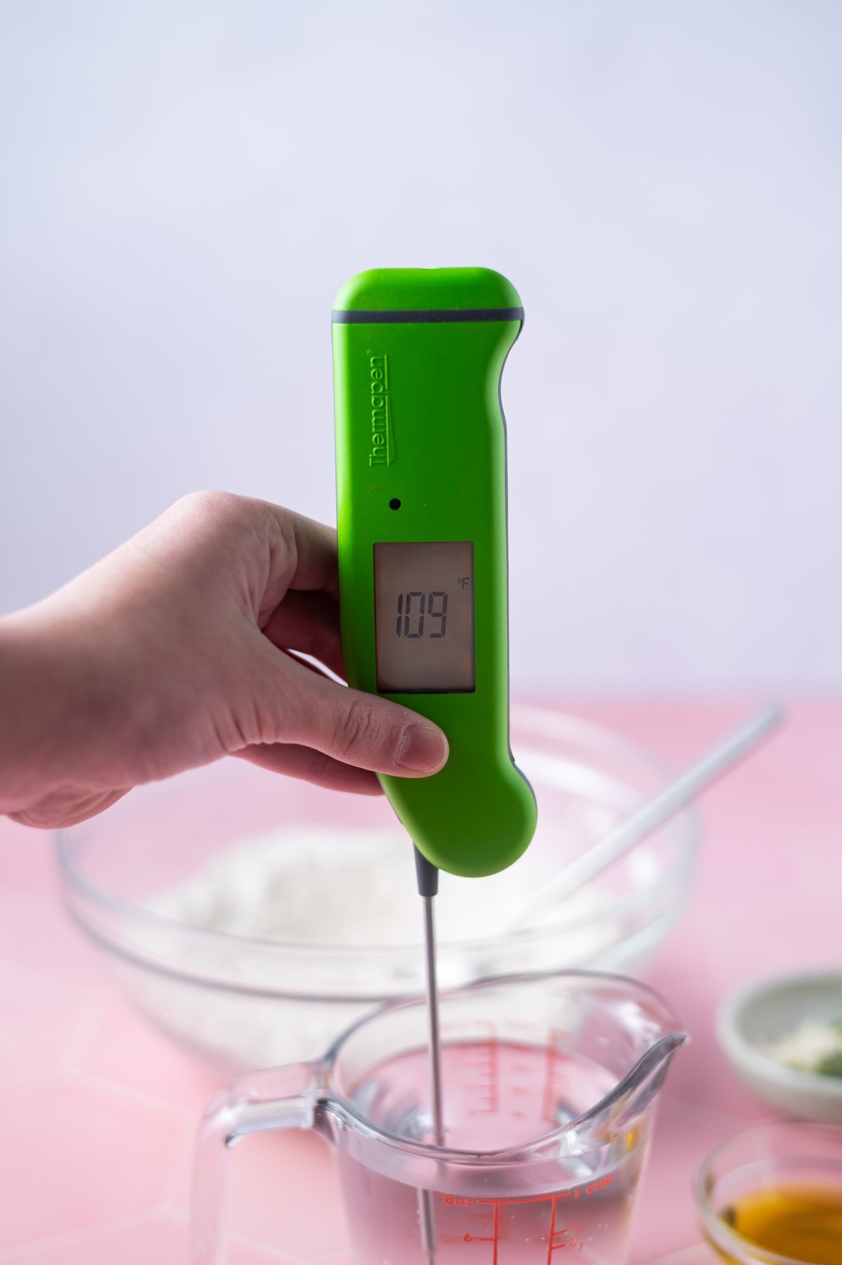 hand holding a thermometer in a measuring cup of water