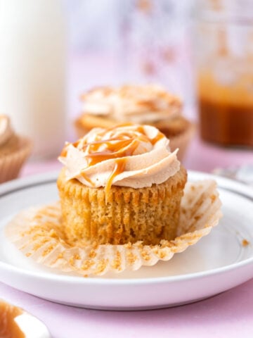 brown butter cupcake on a plate with a spoon of caramel sauce in the foreground and milk and more cupcakes in the background