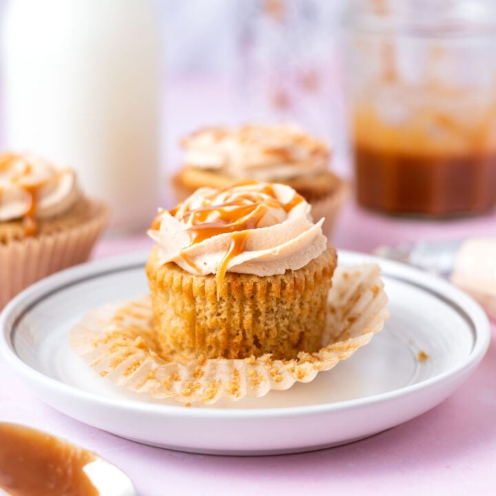 brown butter cupcake on a plate with a spoon of caramel sauce in the foreground and milk and more cupcakes in the background