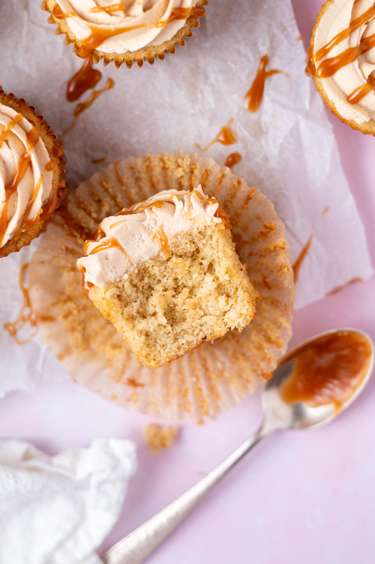 brown butter cupcake in a cupcake liner showing the soft and fluffy texture with a spoon of caramel sauce sitting nearby