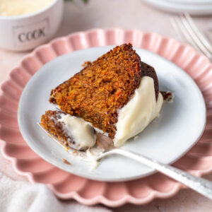 slice of carrot cake on a plate with a bite on a fork