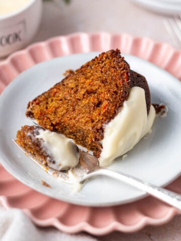 slice of carrot cake on a plate with a bite on a fork