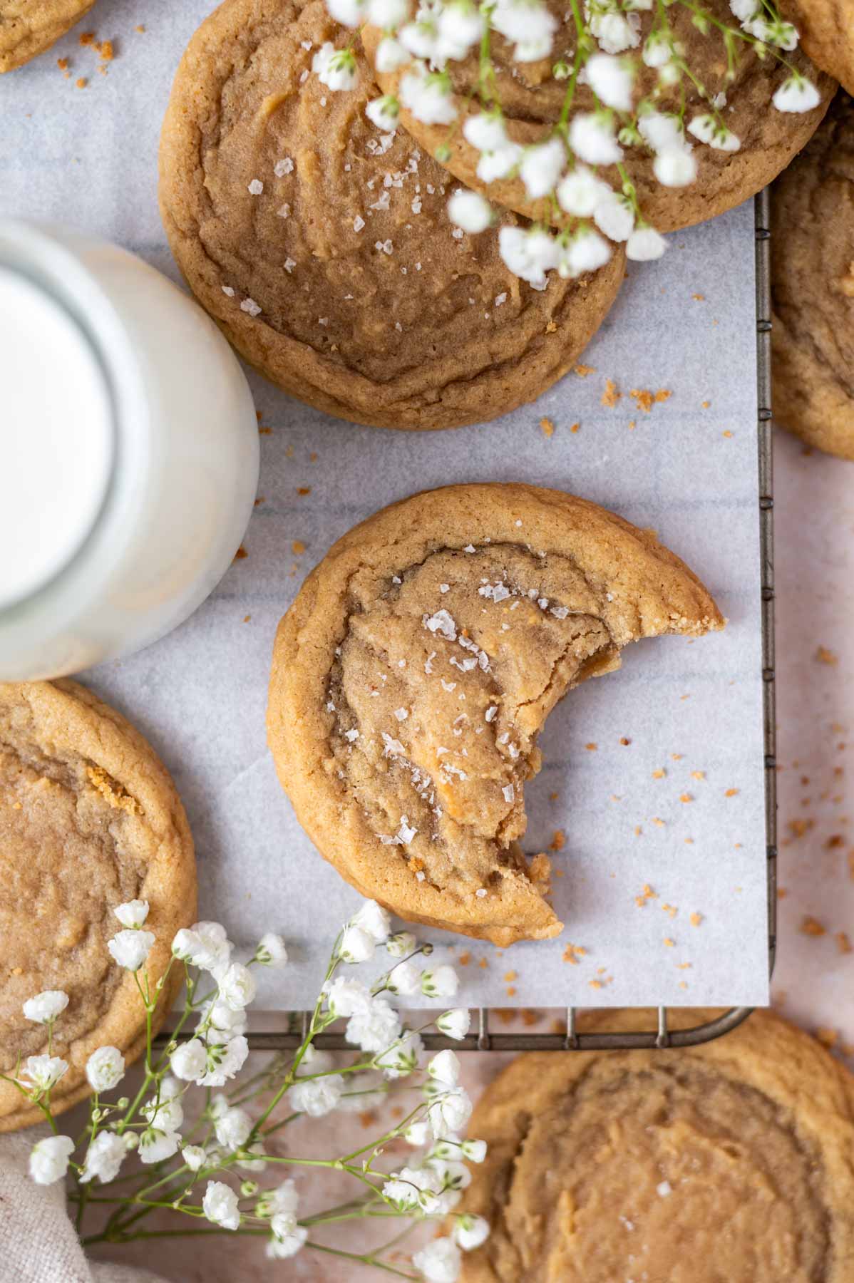 overhead look at a bite missing from a cookie on a parchment lined cooling rack with a glass of milk and baby's breath flowers