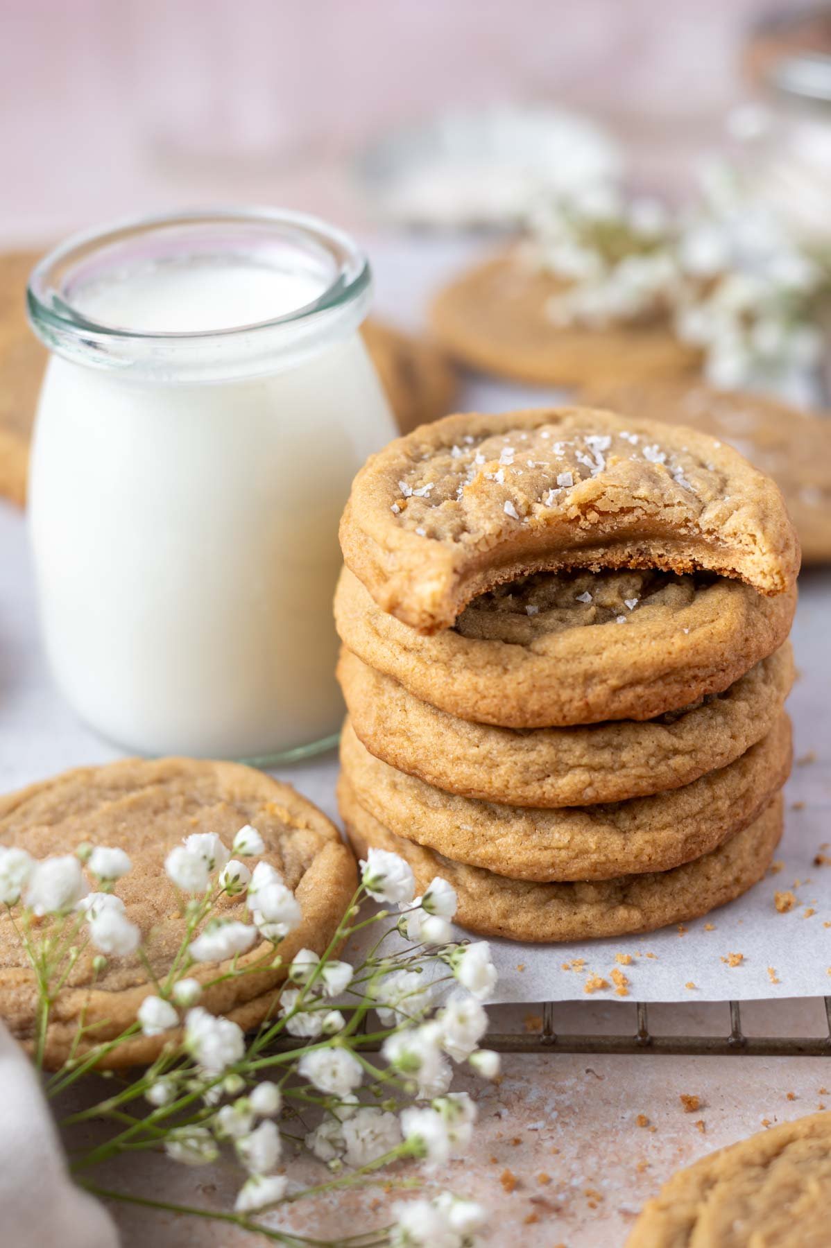 stack of cookies with the top one missing a bite sitting on a parchment lined cooling rack with a glass of milk