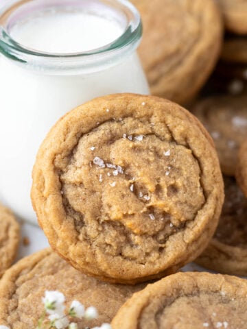 chocolate chipless cookie leaning up against a glass of milk with more cookies piled around