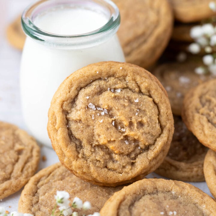 chocolate chipless cookie leaning up against a glass of milk with more cookies piled around