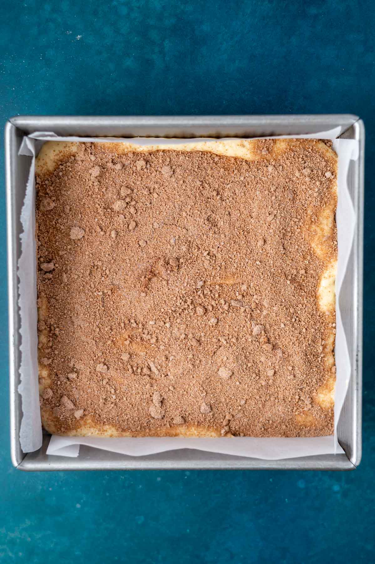 cinnamon filling sprinkled over cake batter in a parchment lined baking pan