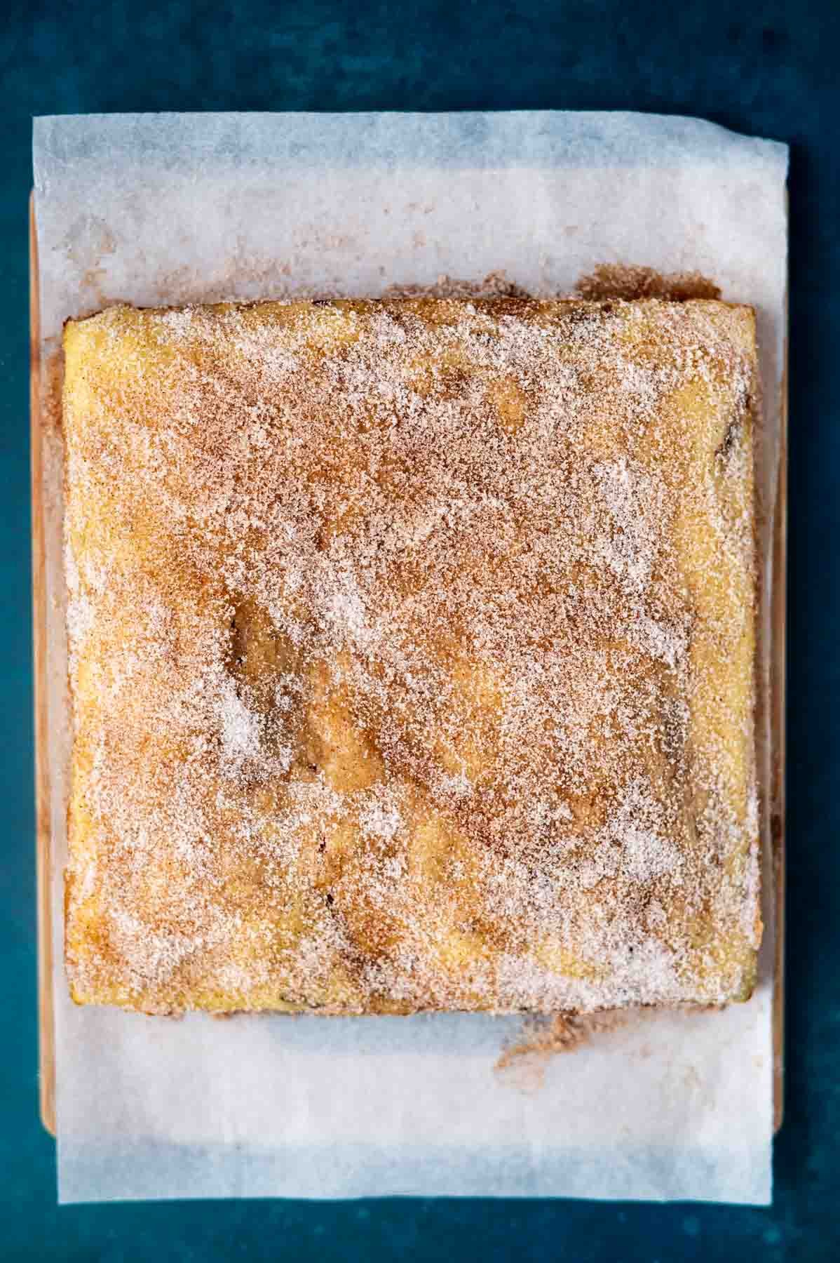 cinnamon sugar coating on top of a churro cake sitting on a parchment lined cutting board