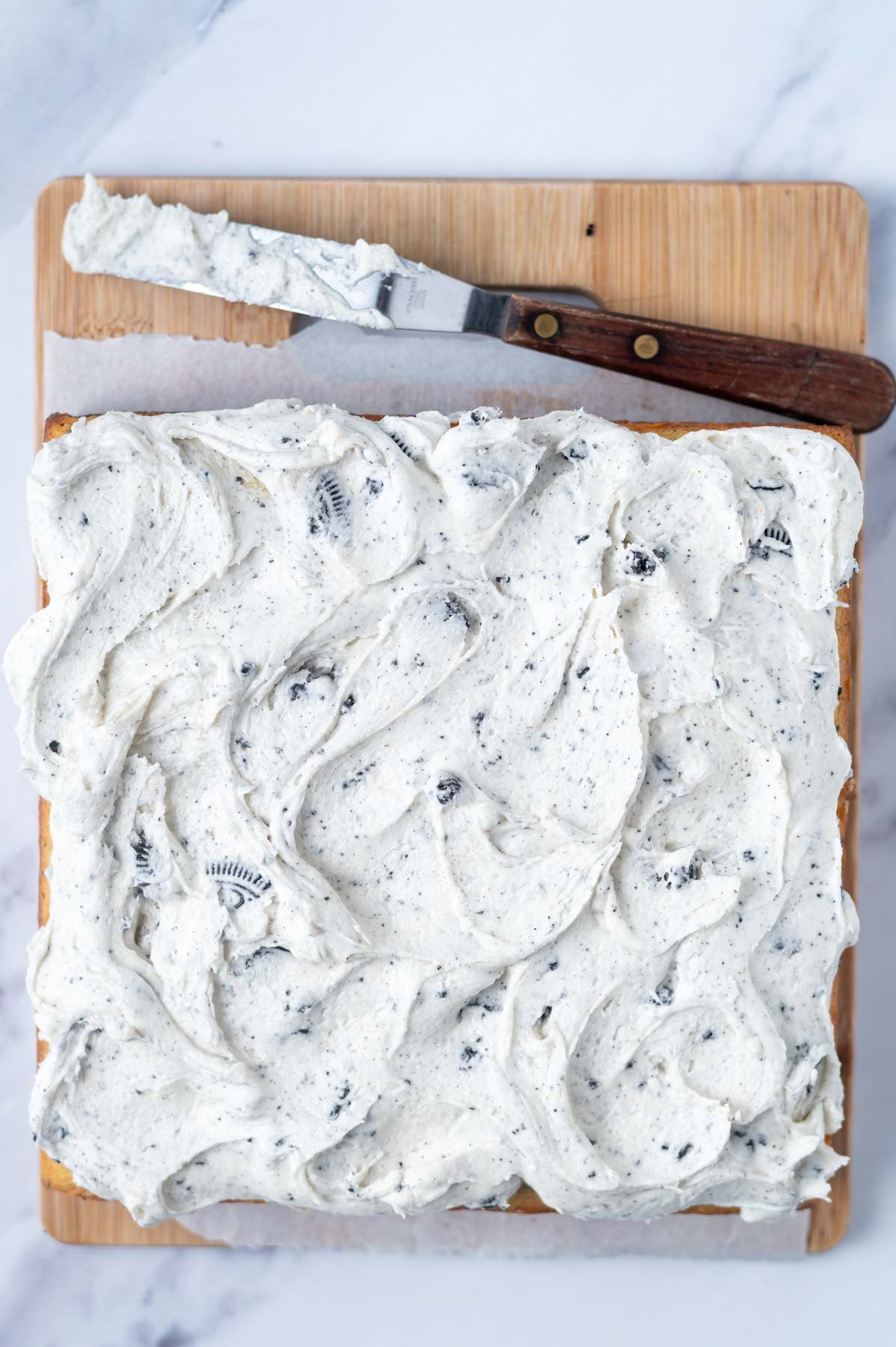 oreo filling frosting over top of cake on a cutting board with an off-set spatula