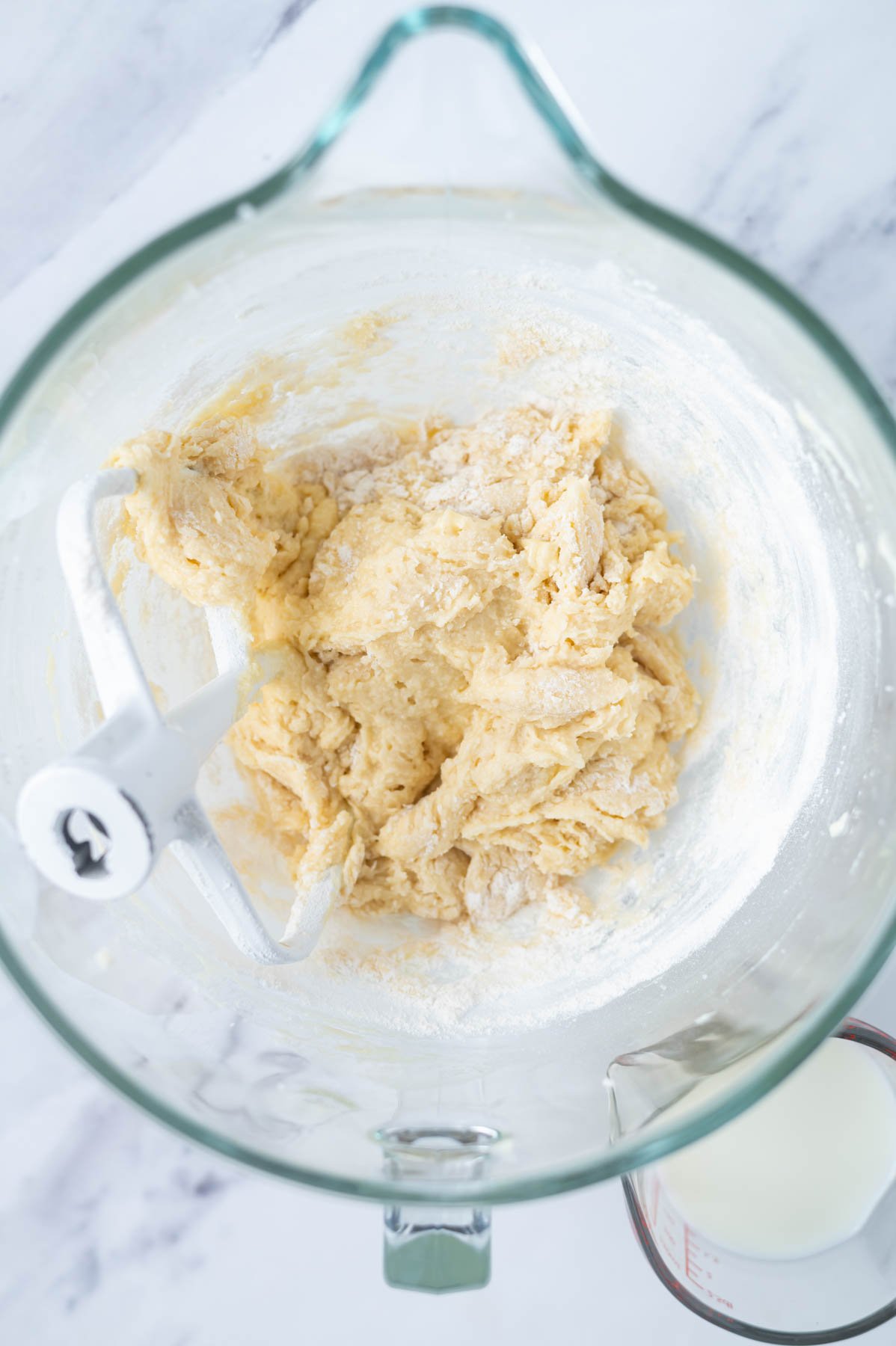 cake batter in a mixing bowl showing some large streaks of flour before the milk is added
