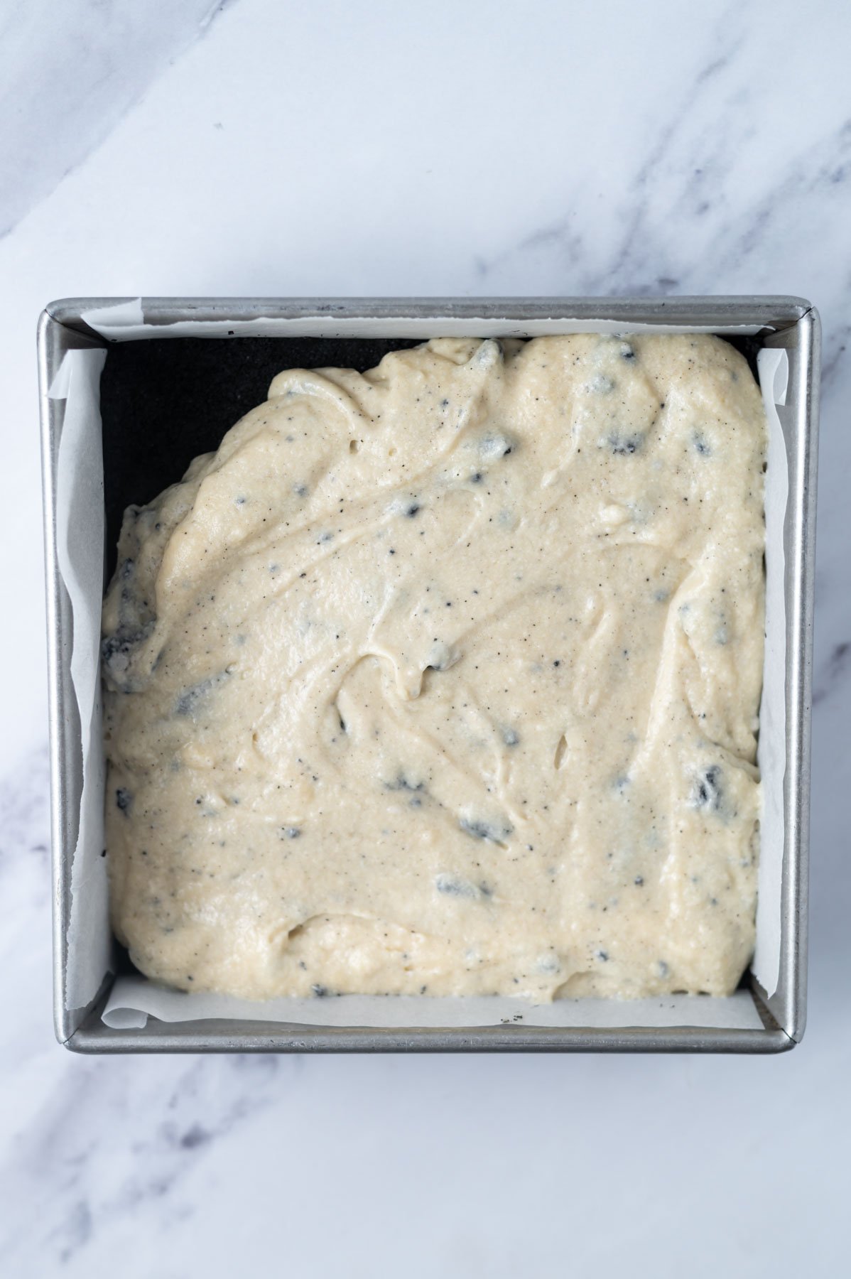 cookies and cream cake batter over cookie crust in a parchment lined baking pan