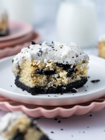 slice of cookies and cream cake on a plate with a piece on a fork and milk in the background