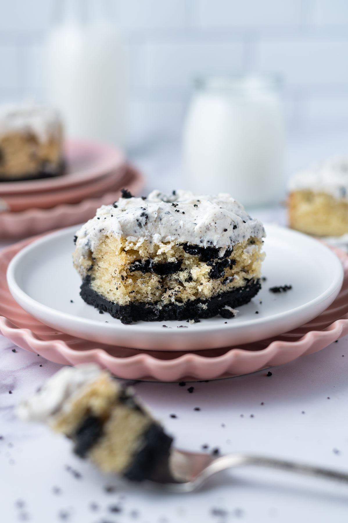 slice of cookies and cream cake on a plate with a piece on a fork and milk in the background