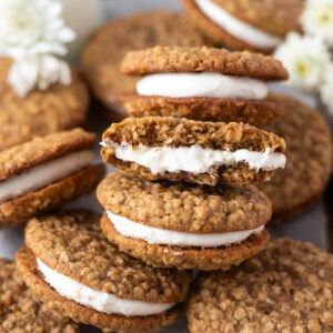 pile of oatmeal cream pie cookies on a parchment lined baking sheet with milk and white flowers in the background
